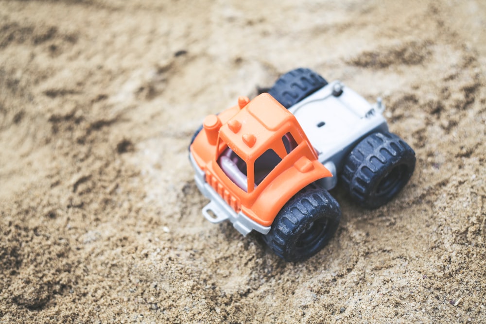 shallow focus photography of orange truck plastic toy on sand